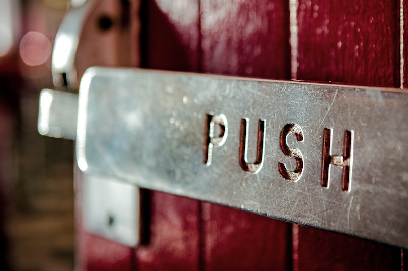Metal hinge with the word PUSH cut out of it on a red door
